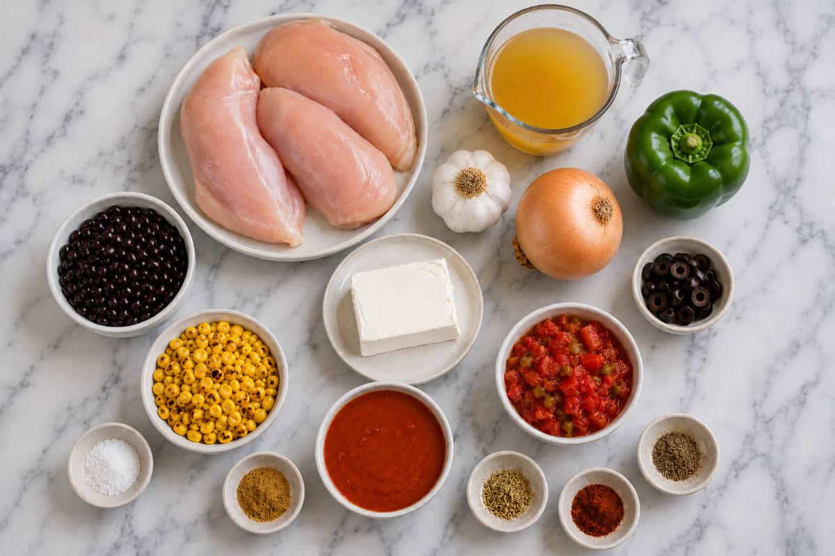 Ingredients for slow cooker chicken enchilada soup arranged on marble: chicken, broth, veggies, beans, cream cheese, and spices.