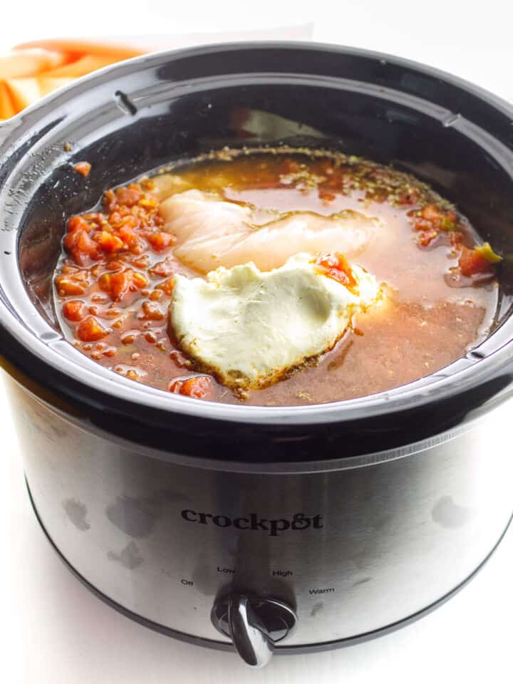 Chicken, tomatoes, broth, seasonings, and cream cheese in a slow cooker for enchilada soup.