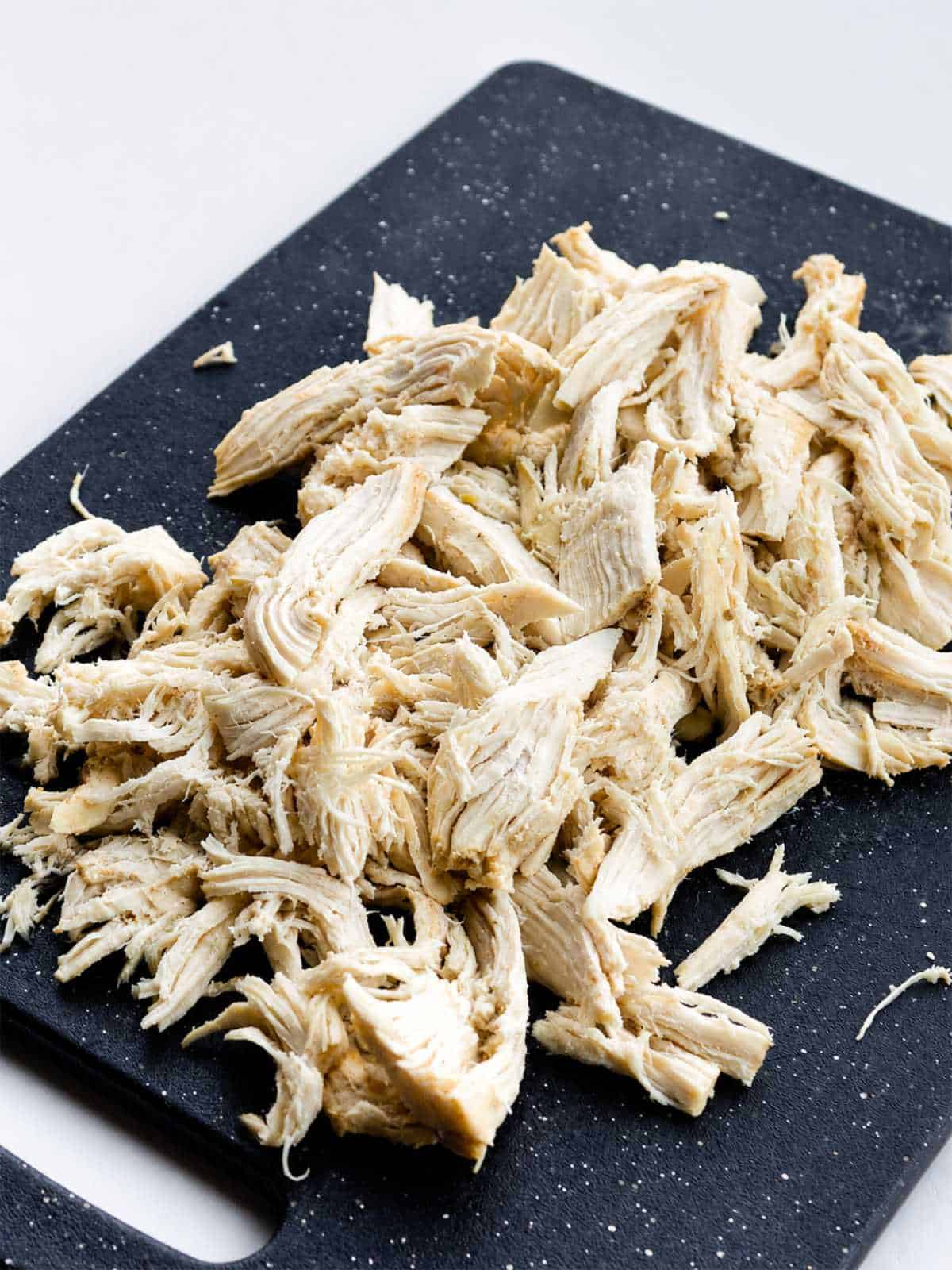 Shredded cooked chicken on a black cutting board for slow cooker chicken enchilada soup.