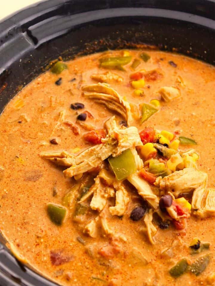 Creamy chicken enchilada soup in a slow cooker with shredded chicken, corn, black beans, peppers, and tomatoes.