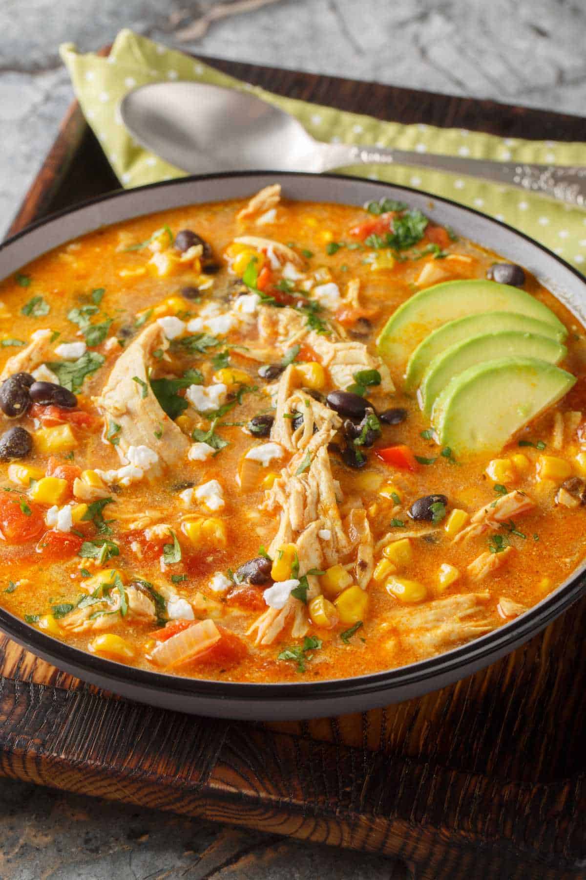 Creamy chicken enchilada soup topped with avocado, cilantro, cheese, and tortilla strips.