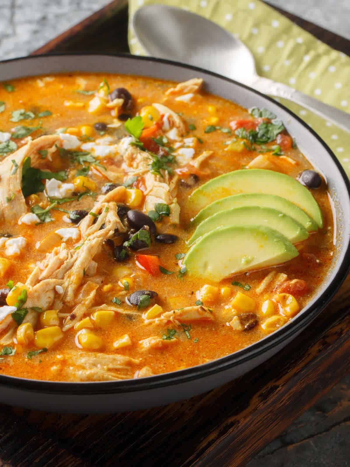 Bowl of creamy chicken enchilada soup with toppings, spoon, and green napkin.