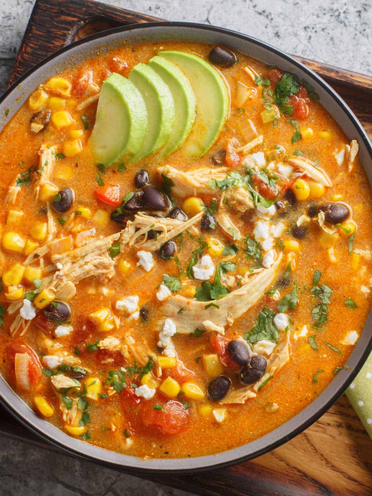 Bowl of slow cooker chicken enchilada soup with avocado, black beans, corn, tomato, and cilantro.