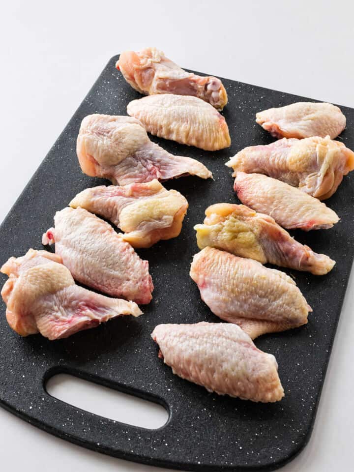 Raw chicken wings lined on a black cutting board for soy garlic chicken wings.