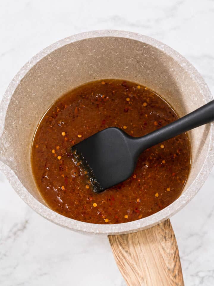 Honey soy garlic glaze simmering in a saucepan with red pepper flakes and a black spatula.