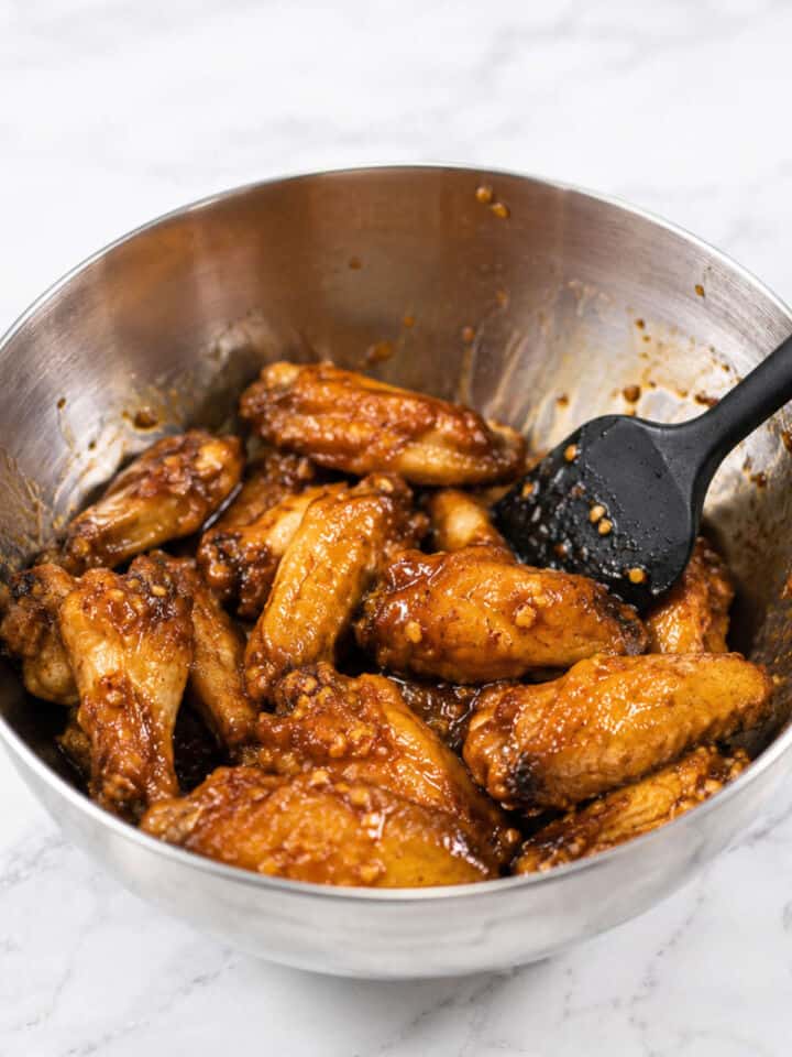 Baked chicken wings tossed with Korean-style soy garlic sauce in a stainless steel bowl.