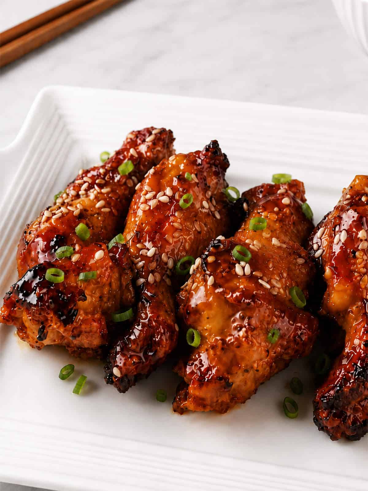 Soy garlic chicken wings with sesame seeds and sliced green onions on a white platter.
