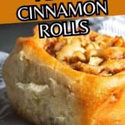 Close-up of a golden apple cinnamon roll with visible apple chunks and cinnamon, on a plate. Text reads “sticky gooey apple cinnamon rolls.”.