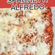 Baked spaghetti Alfredo with melted cheese in a casserole dish on a plaid cloth, with text reading "Baked Spaghetti Alfredo.