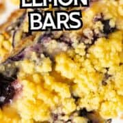 Close-up of golden-topped blueberry lemon bars with juicy blueberries. Text overlay: “Blueberry Lemon Bars.” Blueberries and crumbs in the background.