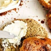 Sliced cinnamon crunch bagel with cream cheese, more bagels, and a cream cheese container on a white surface.