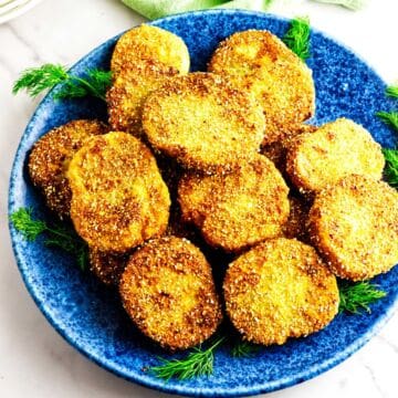 Blue plate with golden fried green tomato slices and dill on a white surface.