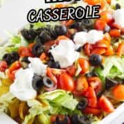 Walking taco casserole in a white dish, topped with shredded lettuce, diced tomatoes, black olives, and sour cream. Text above says "Walking Taco Casserole.