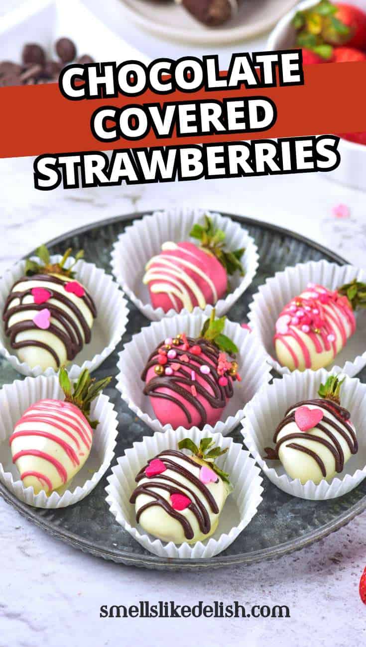 Seven chocolate-covered strawberries with colorful drizzles and heart sprinkles sit in white paper cups on a round tray. Text reads