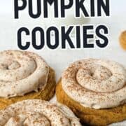 Pumpkin cookies with cinnamon frosting and a dusting of cinnamon on a white surface, partially showing a glass of milk.