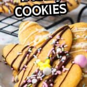 Easter bunny cookies with chocolate drizzle, sprinkles, and candies on a plate; more cookies cool on a rack behind. Text says “Easter Bunny Cookies.”.