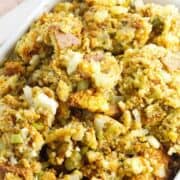Golden Jiffy cornbread dressing with celery and onions in a white dish, serving spoon inside; bold text reads “JIFFY CORNBREAD DRESSING.”.
