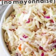 Bowl of creamy old fashioned coleslaw with shredded cabbage, carrots, and purple cabbage, labeled “no mayonnaise.”.