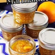Four glass jars of orange marmalade on a blue and white tile, one open to reveal marmalade. An orange is in the background. Text says “Orange Marmalade.”.