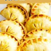 Golden peach hand pies with browned crusts and vent slits on a white plate, topped by a “PEACH HAND PIES” sign.