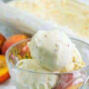 Peach ice cream with peach slices in a glass bowl, in front of a pan of ice cream and whole peaches. The image text says “Peach Ice Cream.”.