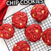 Six red velvet chocolate chip cookies cool on a black wire rack over a white surface, with a red cloth in the background. Text: “Red Velvet Chocolate Chip Cookies.”.