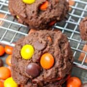 Chocolate cookies with Reese’s Pieces on a cooling rack, extra candies scattered nearby. Bold text says “HALLOWEEN REESE’S PIECES CHOCOLATE COOKIES.”.