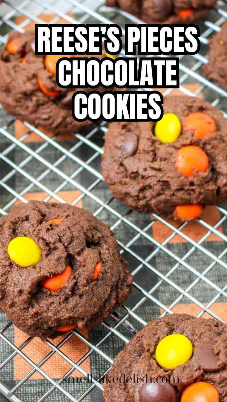 Chocolate cookies topped with orange and yellow Reese's Pieces cool on a wire rack. Bold text: