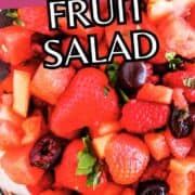 Colorful fruit salad with watermelon, strawberries, cherries, apples, and mint in a glass bowl; overlay text reads “WATERMELON FRUIT SALAD.”.