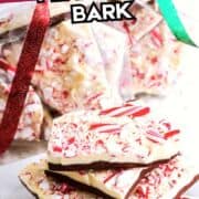 Stacked white chocolate peppermint bark on a plate, with more in ribbon-tied gift bags behind. Text overlay: “White Chocolate Peppermint Bark.”.